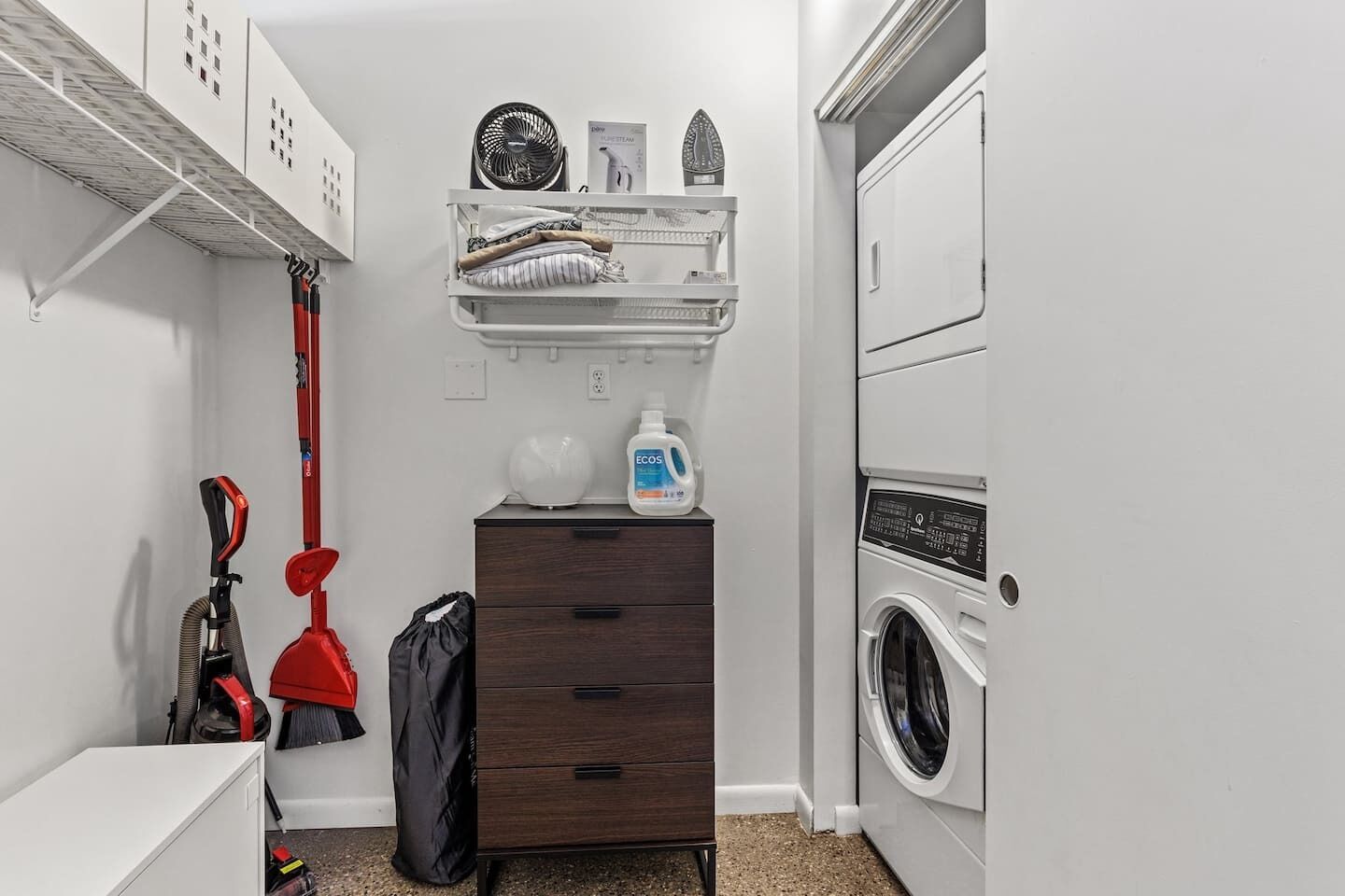 Une buanderie équipée d’un lave-linge, d’un étendoir, d’un aspirateur et d’un meuble de rangement.