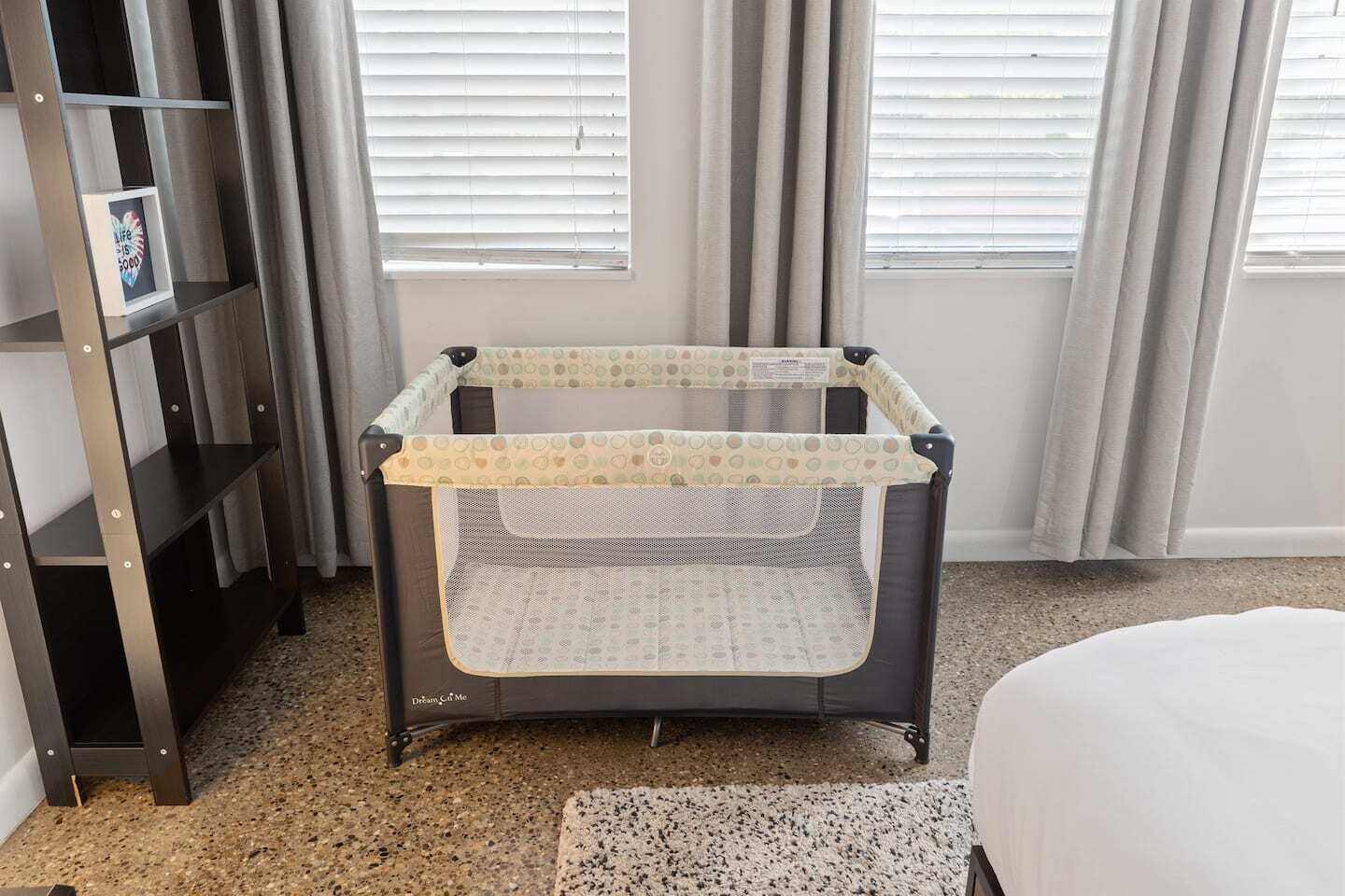 A baby crib with a mesh cover in a room with a bookshelf and a window with curtains.
