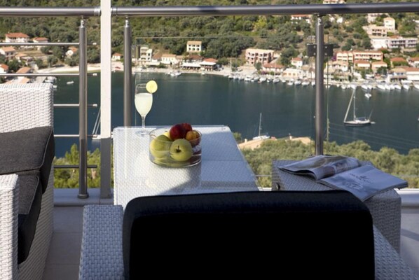 A balcony with wicker furniture, a table with fruit and a glass of white wine, overlooking a marina with boats and buildings. - Villa Faneromeni in Lefkada (Lefkada)