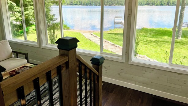 A room with large windows overlooking a lake, a wooden bench, and a view of a grassy area with a bench and a dock.