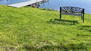 A grassy area with a dock extending into a calm lake, surrounded by trees.