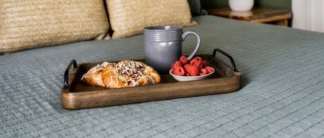 Una cama con un edredón gris, una bandeja de madera con un pastel, frambuesas y una taza gris.