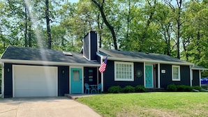 Une maison de plain-pied avec un garage, une véranda à l’avant avec une petite table et des chaises, et un drapeau américain.
