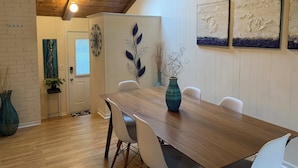 Un coin repas avec une table en bois, des chaises blanches et un vase bleu.