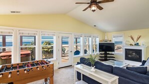 Ein Wohnzimmer mit Fußballtisch, Fernseher, Kamin und großen Fenstern mit Meerblick.