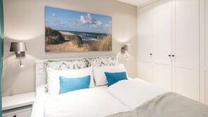 A bedroom with a bed, two wall-mounted lamps, a large beach painting, and a wardrobe. - Loddis Hüs - Loddi's Hüs (Wenningstedt-Braderup (Sylt))