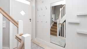 A modern hallway with a wooden staircase, a door with a mirror, and a coat rack with hooks. - Loddis Hüs - Loddi's Hüs (Wenningstedt-Braderup (Sylt))