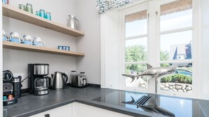 A modern kitchen with stainless steel appliances, wooden shelves, and a view of a shark sculpture outside. - Loddis Hüs - Loddi's Hüs (Wenningstedt-Braderup (Sylt))