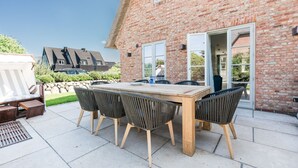 An outdoor patio with a wooden table and chairs, a white deck chair, and a stone wall. - Loddis Hüs - Loddi's Hüs (Wenningstedt-Braderup (Sylt))