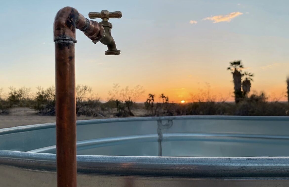 A sunset view with a swimming pool and a faucet in the foreground.