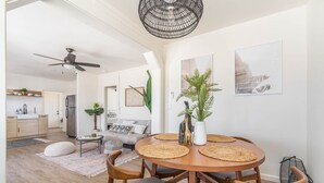 Ein modernes Wohnzimmer mit einem runden Holzesstisch, grau gepolsterten Stühlen, einem Deckenventilator und einem großen Fenster.