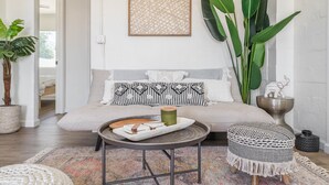 Ein gemütliches Wohnzimmer mit einer Couch, einem Couchtisch und einem Beistelltisch. Eine große Pflanze und ein gerahmtes Kunstwerk sind an der Wand zu sehen.