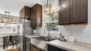A modern kitchen with stainless steel appliances, dark wooden cabinets, a large window, and a hanging light fixture.