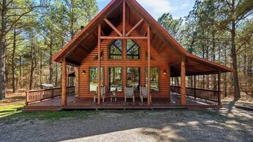 A wooden cabin with a triangular roof, large windows, and a covered porch with seating.