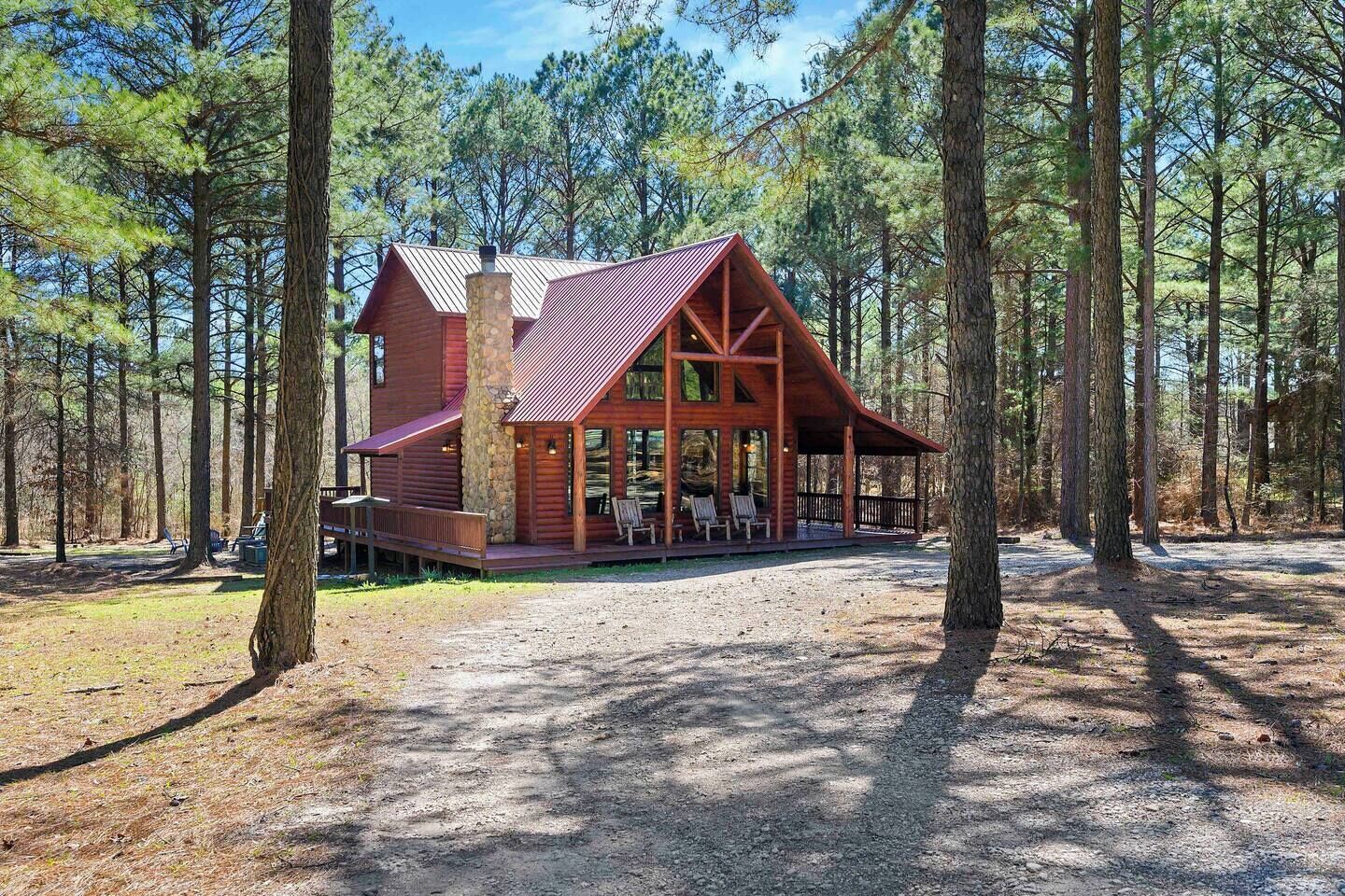 A rustic cabin with a stone chimney, large windows, and a covered porch with seating.