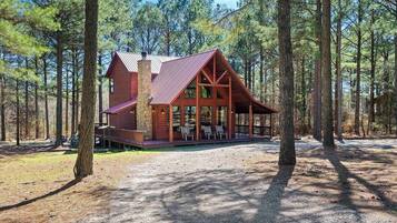 A rustic cabin with a stone chimney, large windows, and a covered porch with seating.