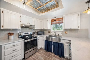 A modern kitchen with white cabinetry, stainless steel appliances, and a wooden floor.