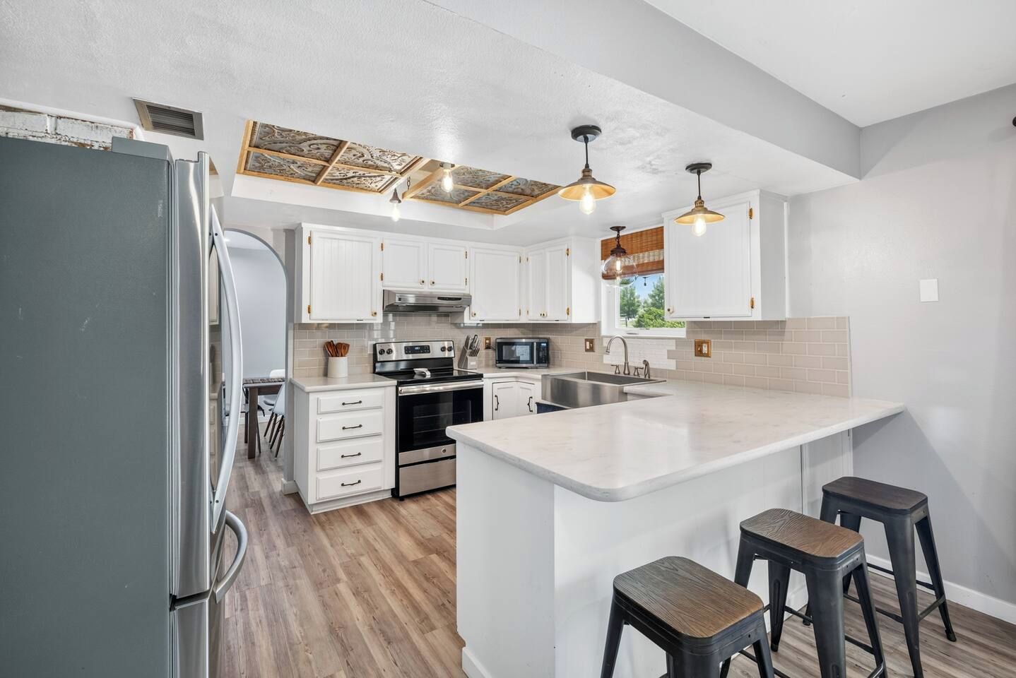 Una cocina moderna con armarios blancos, electrodomésticos de acero inoxidable y una isla central con taburetes.