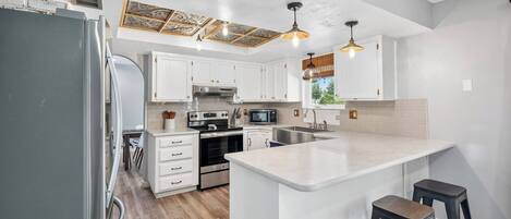 Una cocina moderna con armarios blancos, electrodomésticos de acero inoxidable y una isla central con taburetes.