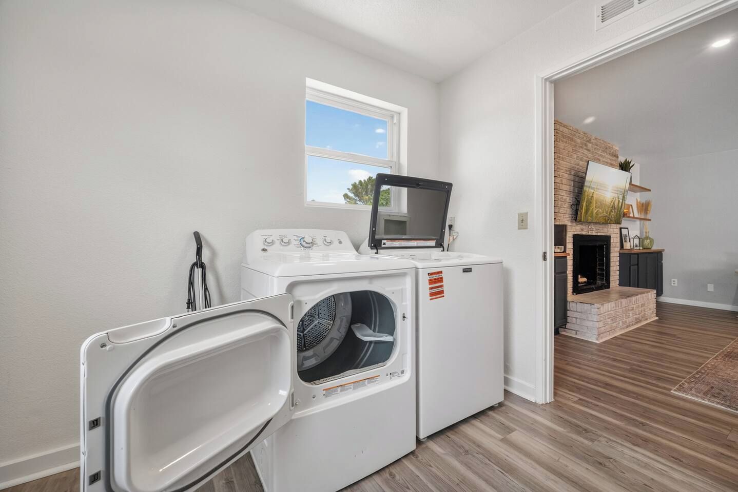 A laundry room with a washer and dryer, a window, and a fireplace in the adjacent living area.