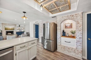 Une cuisine moderne avec un réfrigérateur en acier inoxydable, des meubles blancs et un mur d’accent en briques.