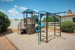 A playground with a climbing structure, a slide, and a covered area.