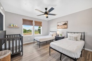 A bedroom with two beds, a crib, a ceiling fan, and a window with a view. - Hummingbird House - 2 King Beds, Mountain Views & Fire Pit (Sierra Vista)