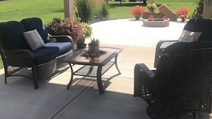 Un patio techado con mobiliario exterior, una chimenea y vistas a un campo cubierto de hierba.