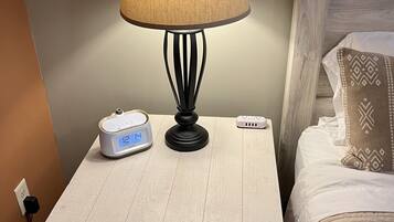 Een nachtkastje met een lamp, een klok en een stekkerdoos.