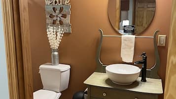 A bathroom with a toilet, sink, and mirror. There is a 'Welcome' sign and a 'No Smoking' sign on the wall.