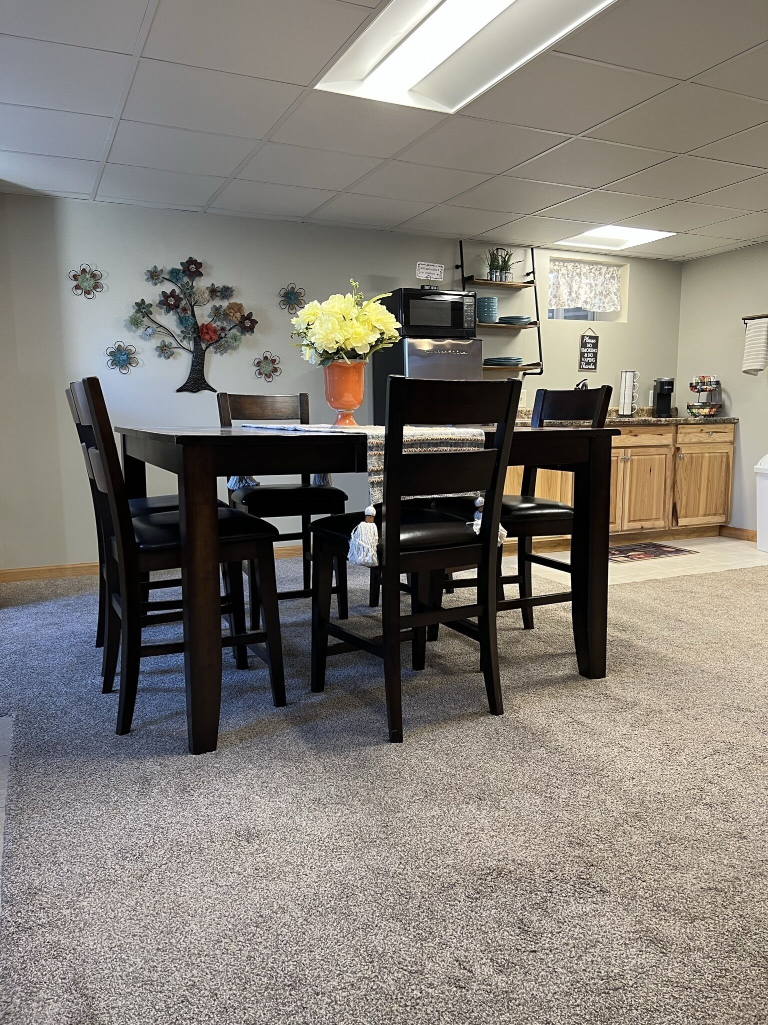 A dining area with a table and chairs, a vase with flowers, a microwave, and a coffee maker on the counter.