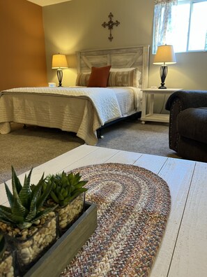 A bedroom with a bed, two bedside lamps, a dark armchair, a woven rug, and a small potted plant. - Private Large Suite, cozy, quiet & close to I-75 (Lebanon)