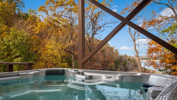 Een hottub met uitzicht op herfstbomen en een houten terras.