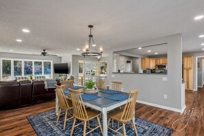 A spacious dining area with a large table, wooden chairs, and a chandelier. - 🌊Lakefront Hot Tub🛶Kayaks🔥Firepit🏖️Nature Lovers🦅Peaceful waterfront deck (Bull Shoals)