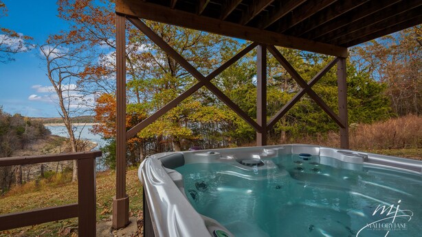 A hot tub under a wooden pergola with a view of a lake and autumn trees. - 🌊Lakefront Hot Tub🛶Kayaks🔥Firepit🏖️Nature Lovers🦅Peaceful waterfront deck (Bull Shoals)