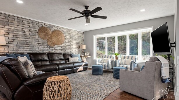 A modern living room with a leather sofa, a grey armchair, a flat-screen TV, and a large window offering a view of greenery. - 🌊Lakefront Hot Tub🛶Kayaks🔥Firepit🏖️Nature Lovers🦅Peaceful waterfront deck (Bull Shoals)