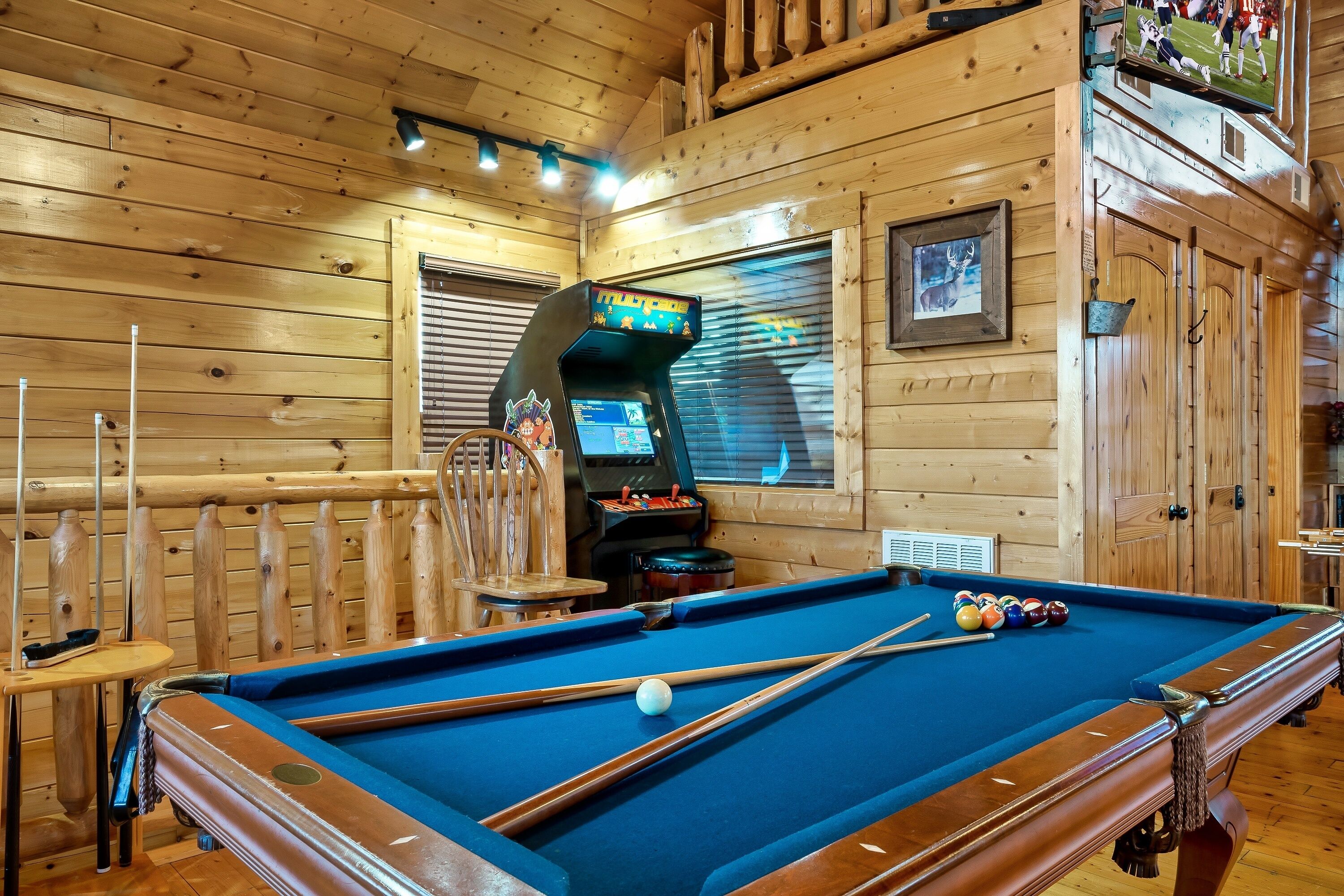 A pool table with pool cues and balls, a pool table chair, and a jukebox in a wooden room with a wooden ceiling and walls.
