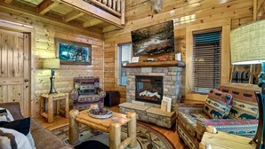 A cozy log cabin interior with a stone fireplace, wooden furniture, and a deer head decoration. - SPRING DISCOUNTS! Hot Tub ⭐️ AMAZING VIEWS⭐️ Games 🎱 🐻 (Sevierville)