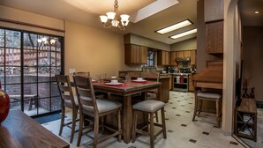 Un comedor con mesa y sillas de madera, una lámpara de araña y vistas a un patio exterior.