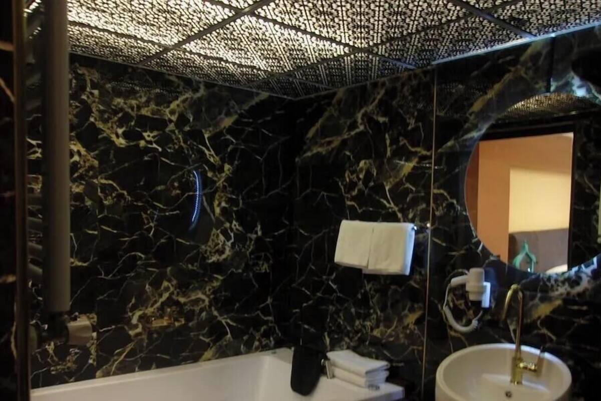 Un baño con pared de mármol, una bañera, un lavamanos y un espejo.