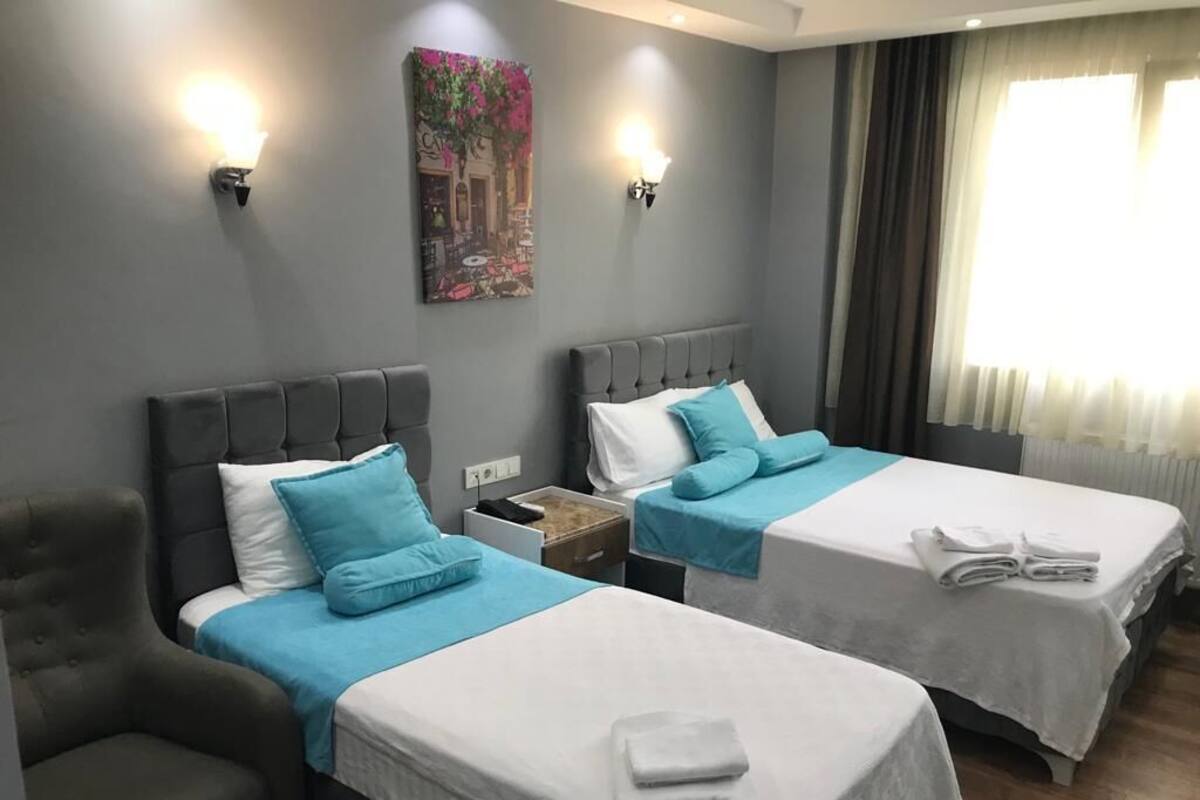 Una habitación de hotel con dos camas, una silla, una mesita de noche y un cuadro en la pared.