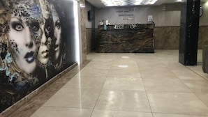 A hotel reception area with a marble counter, a large wall mural, and a ceiling with a geometric pattern.