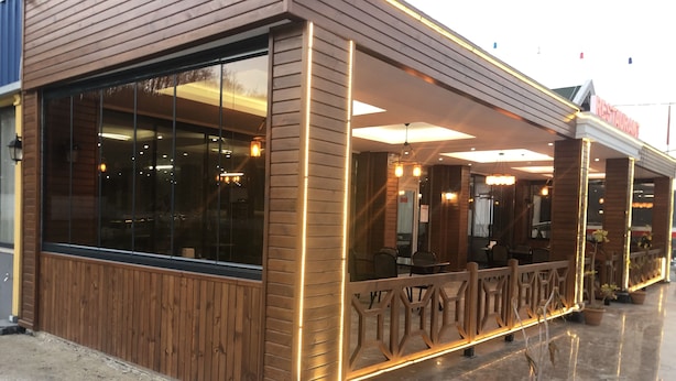 A restaurant with large windows, a wooden facade, and a covered outdoor seating area.
