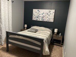 A bedroom with a bed, two bedside tables, a wall-mounted lamp, and a floral artwork.