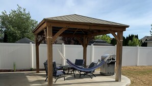 Un patio cubierto con una pérgola de madera, muebles de exterior y un hogar para fuego.
