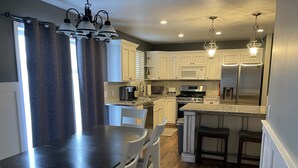 Una cocina moderna con armarios blancos, una encimera oscura y un comedor con mesa y sillas.