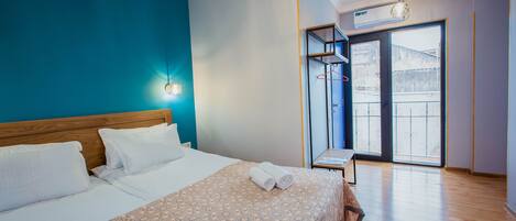 A hotel room with a bed, a nightstand, a window with blinds, and a ceiling-mounted air conditioner.