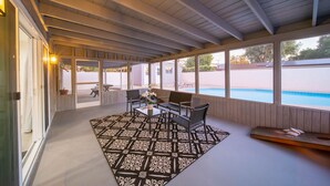 Un porche techado con vista a la piscina, amueblado con asientos y alfombra estampada.