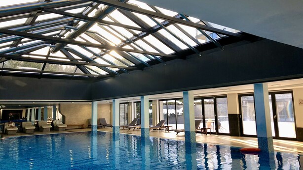 An indoor swimming pool with a skylight ceiling, lounge chairs, and a view of the outside. - Luxury 2BR Penthouse in an elegant hotel with lavish SPA & Heated Swimming Pool (Bansko)