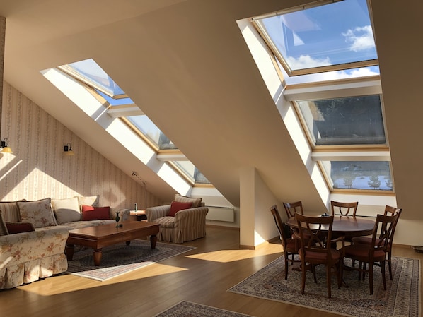 A spacious loft with high ceilings, skylights, a cozy seating area, and a dining table.